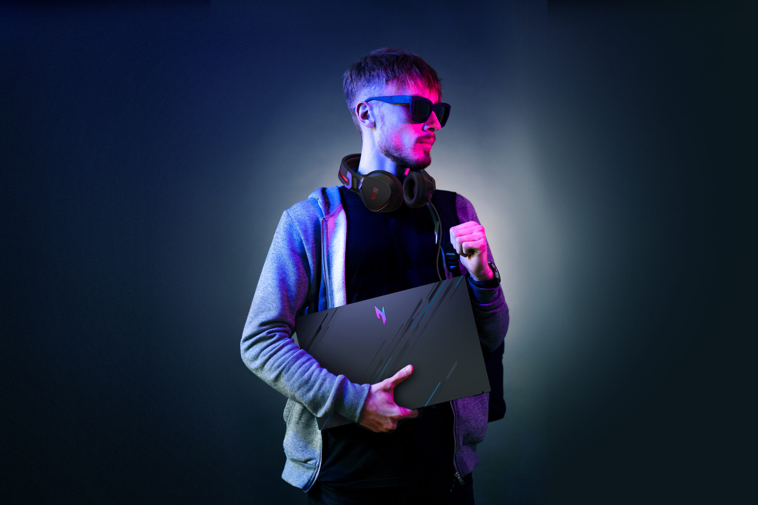 ACER Neon portrait of a bearded man wearing headphones on the neck, parka, backpack, mate sunglasses holding a gamer laptop in hands. Hacker portrait; Shutterstock ID 2077586416; purchase_order: -; job: -; client: -; other: -